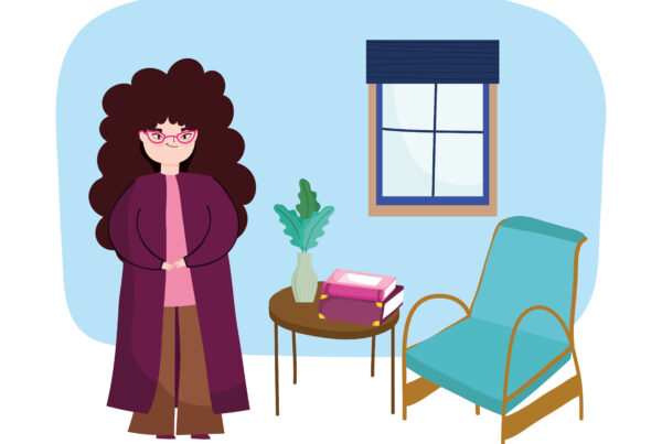 Psychoterapeutka stoi w gabinecie psychologicznym, obok na stoliku leżą książki o nurtach psychoterapii.