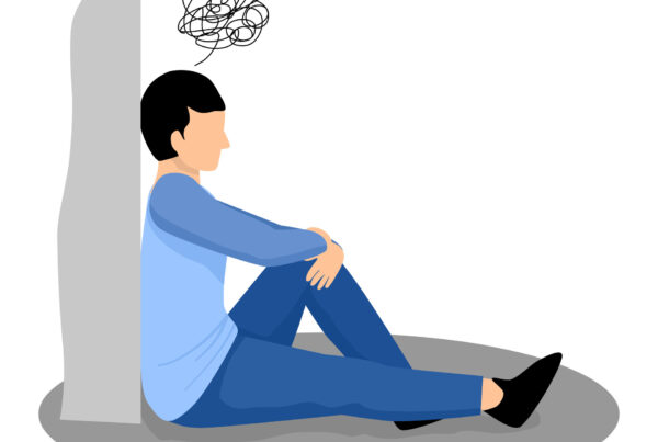 Mężczyzna siedzi pod ścianą, pochłonięty ruminacjami.